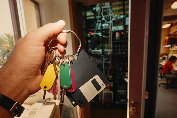 A black hardware security key plugged into a graphite cube computer, a second key and a key ring beside it, one orange-red light